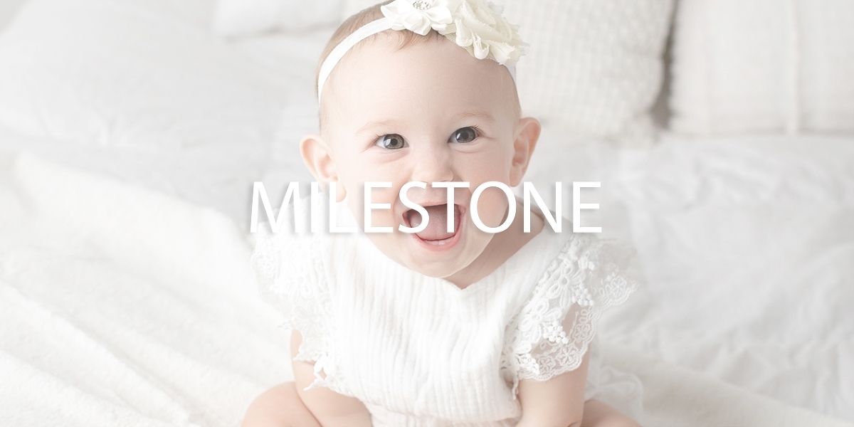 Okotoks AB milestone photography of a baby smiling directly at the camera while wearing white dress by Dana Menenedez